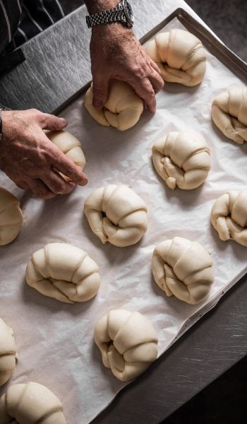 Tray of uncooked croissants, a man's hand rearranges them