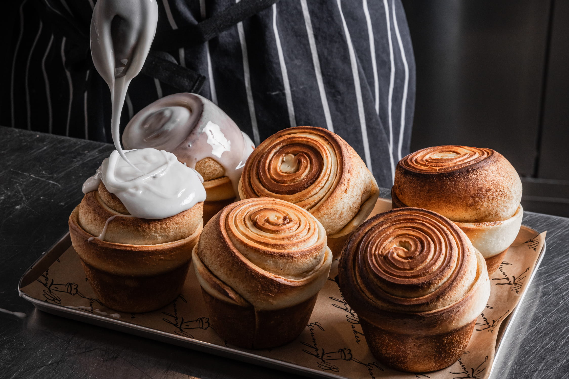 cinnamon scrolls being glazed on a baking tray with white icing
